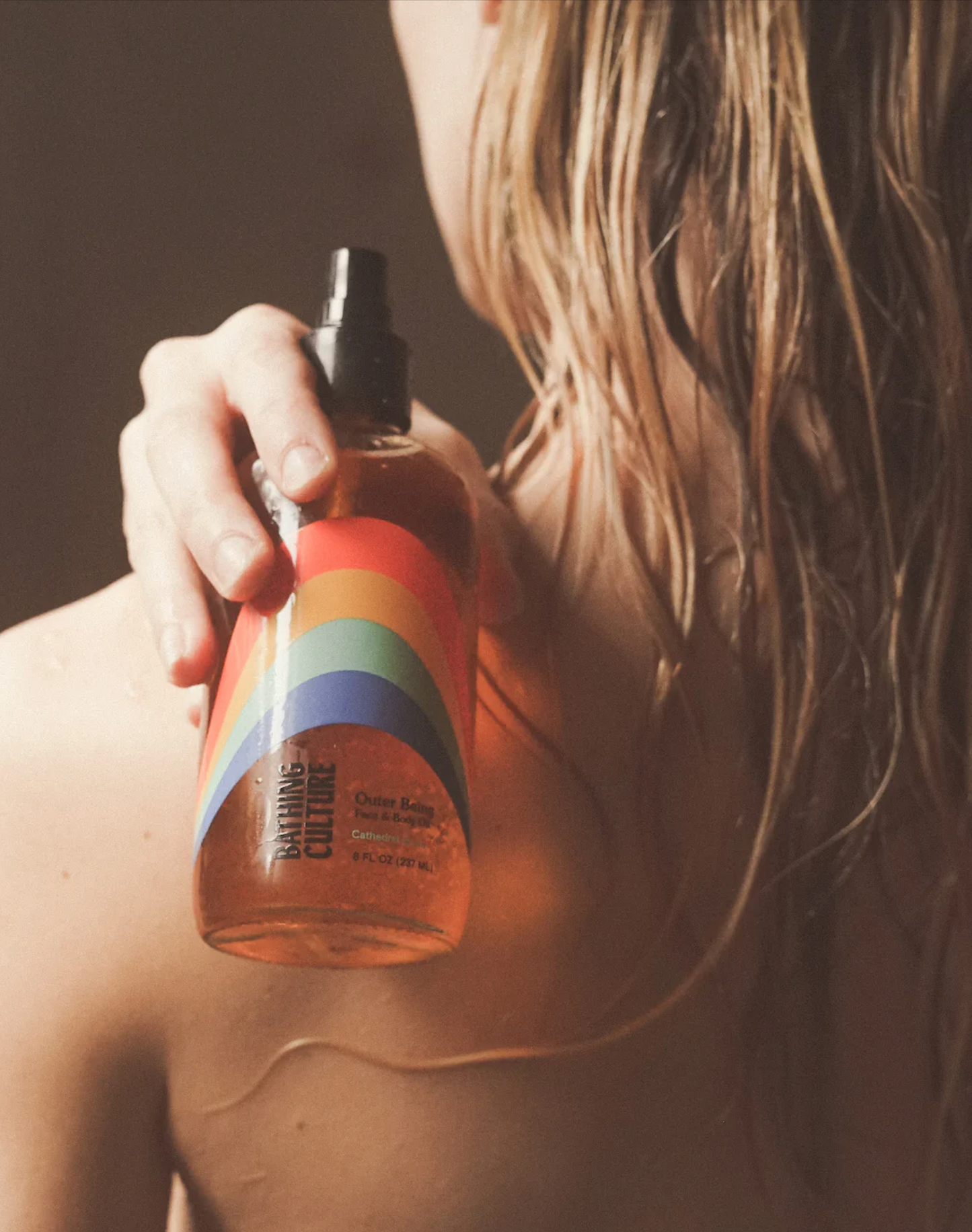 A person holding a bottle of Bathing Culture Outer Being Face & Body Oil, a solar restorative, anti-inflammatory, natural moisture retainer